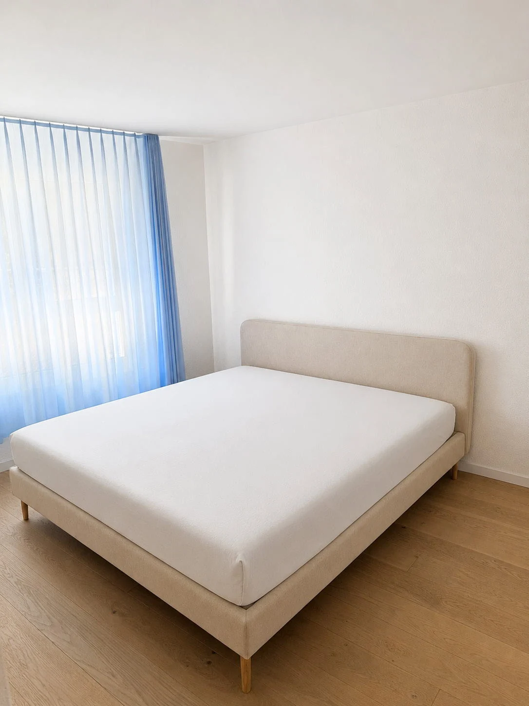 Helles Schlafzimmer mit Parkettboden und Vorhängen